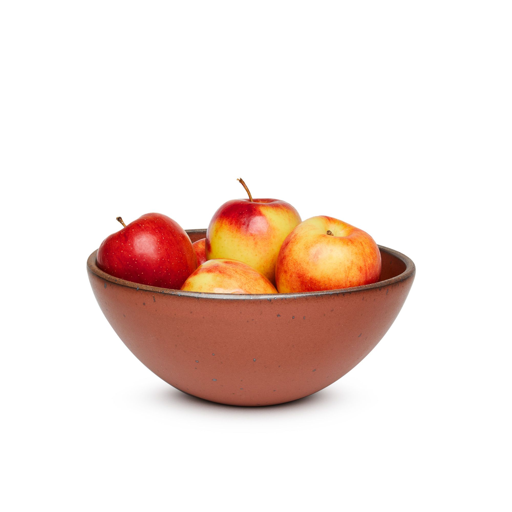 A large rounded ceramic bowl in a cool burnt terracotta color featuring iron speckles and an unglazed rim, filled with apples