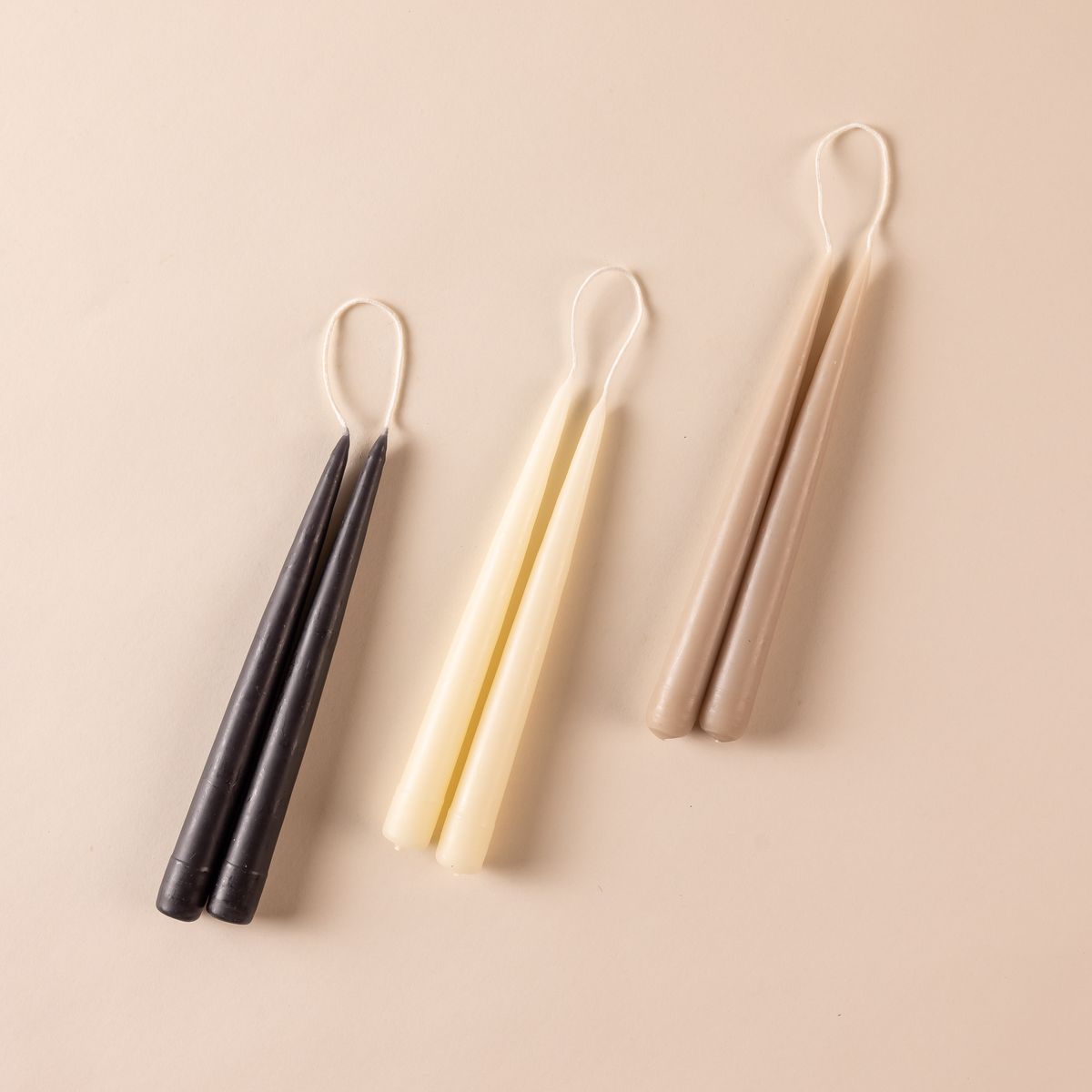 Three pairs of taper candles lined up in black, cream, and taupe colors.