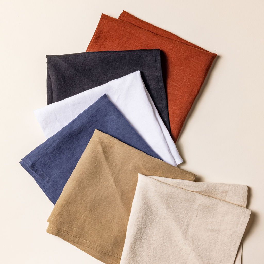 Six folded napkins in terracotta, black, neutral, navy, and white colors arranged and fanned out