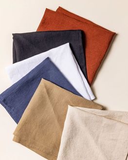 Six folded napkins in terracotta, black, neutral, navy, and white colors arranged and fanned out