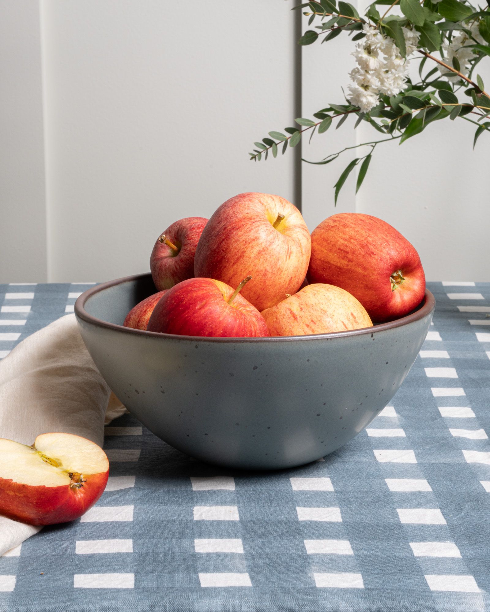 Red apples in a large ceramic mixing bowl in a blue-grey color and on a blue-grey crosshatch tablecloth
