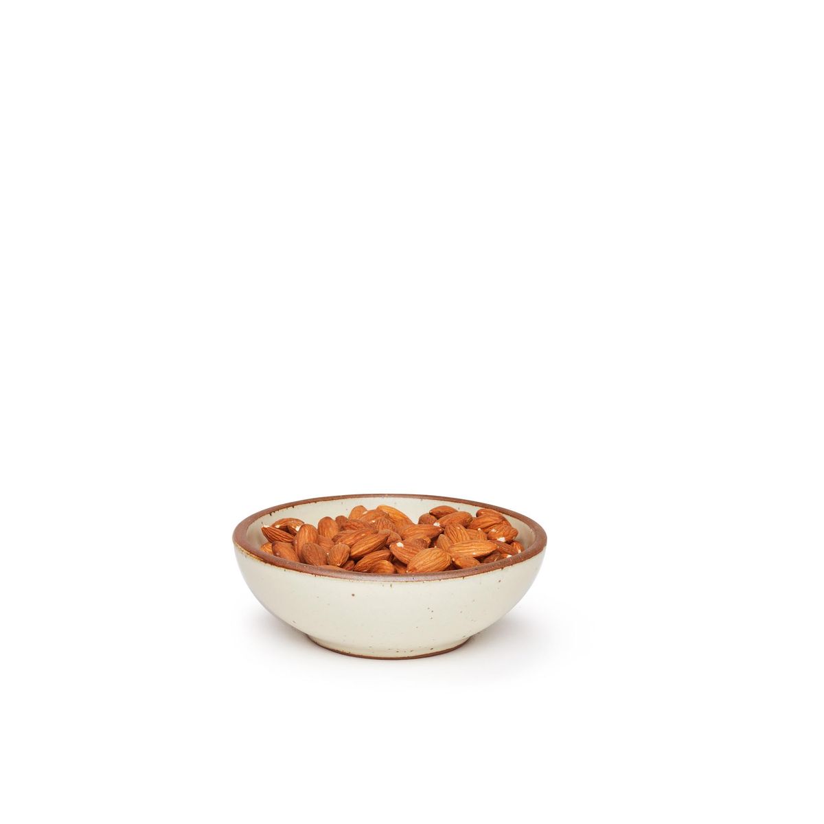 A small shallow ceramic bowl in a warm, tan-toned, off-white color featuring iron speckles and an unglazed rim, filled with almonds