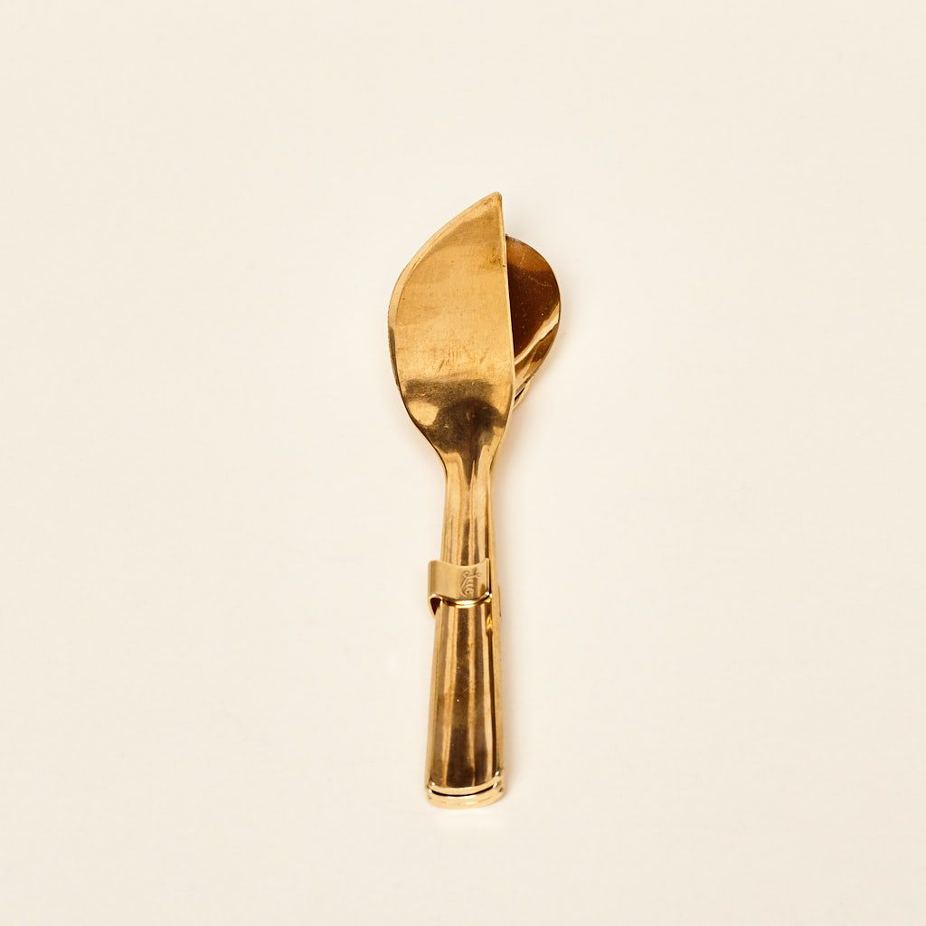 A brass fastener holds a brass knife atop a brass spoon