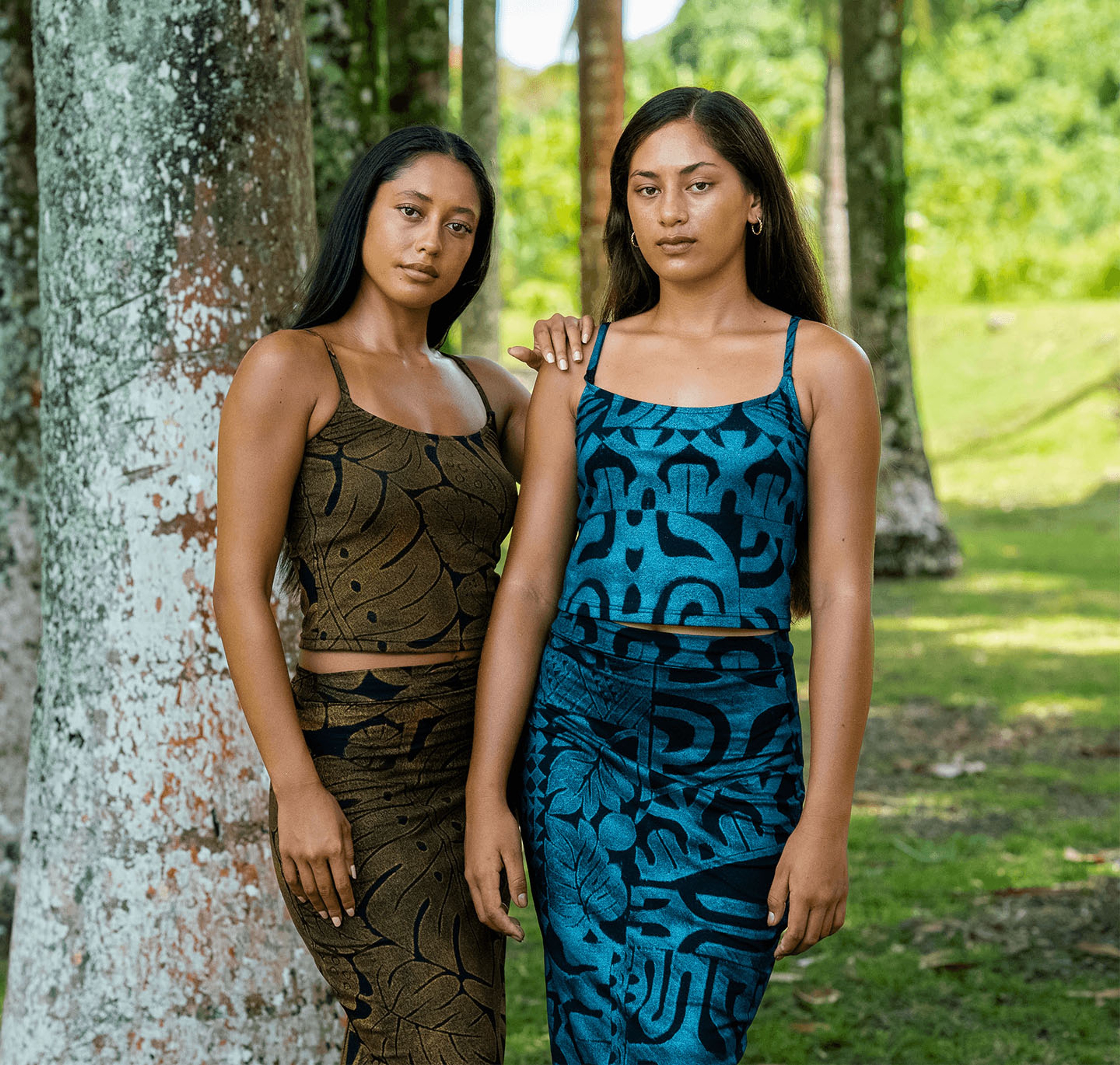 Two women wearing evening dresses standing in a coconut tree grove