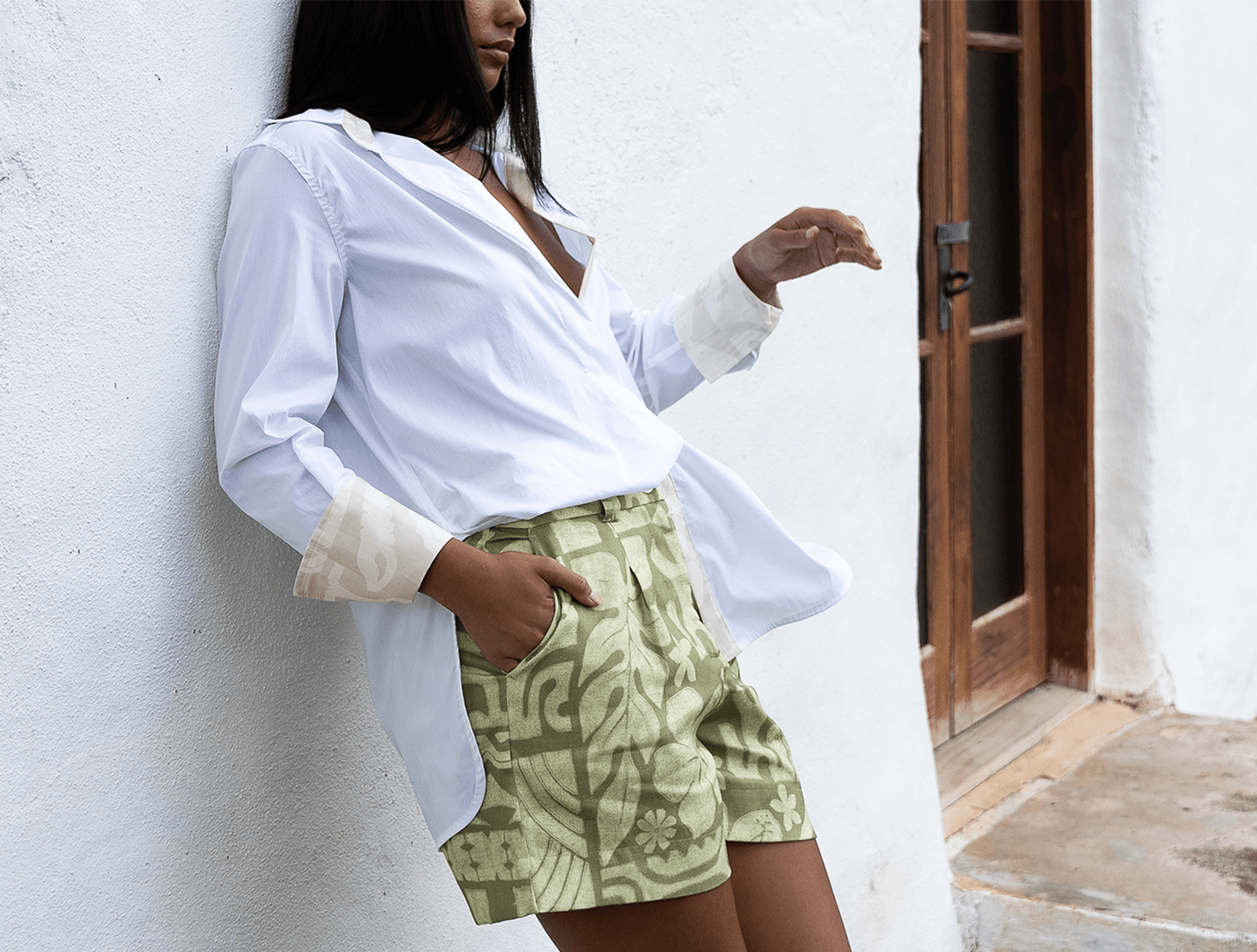 Woman wearing printed green shorts leaning on a white wall