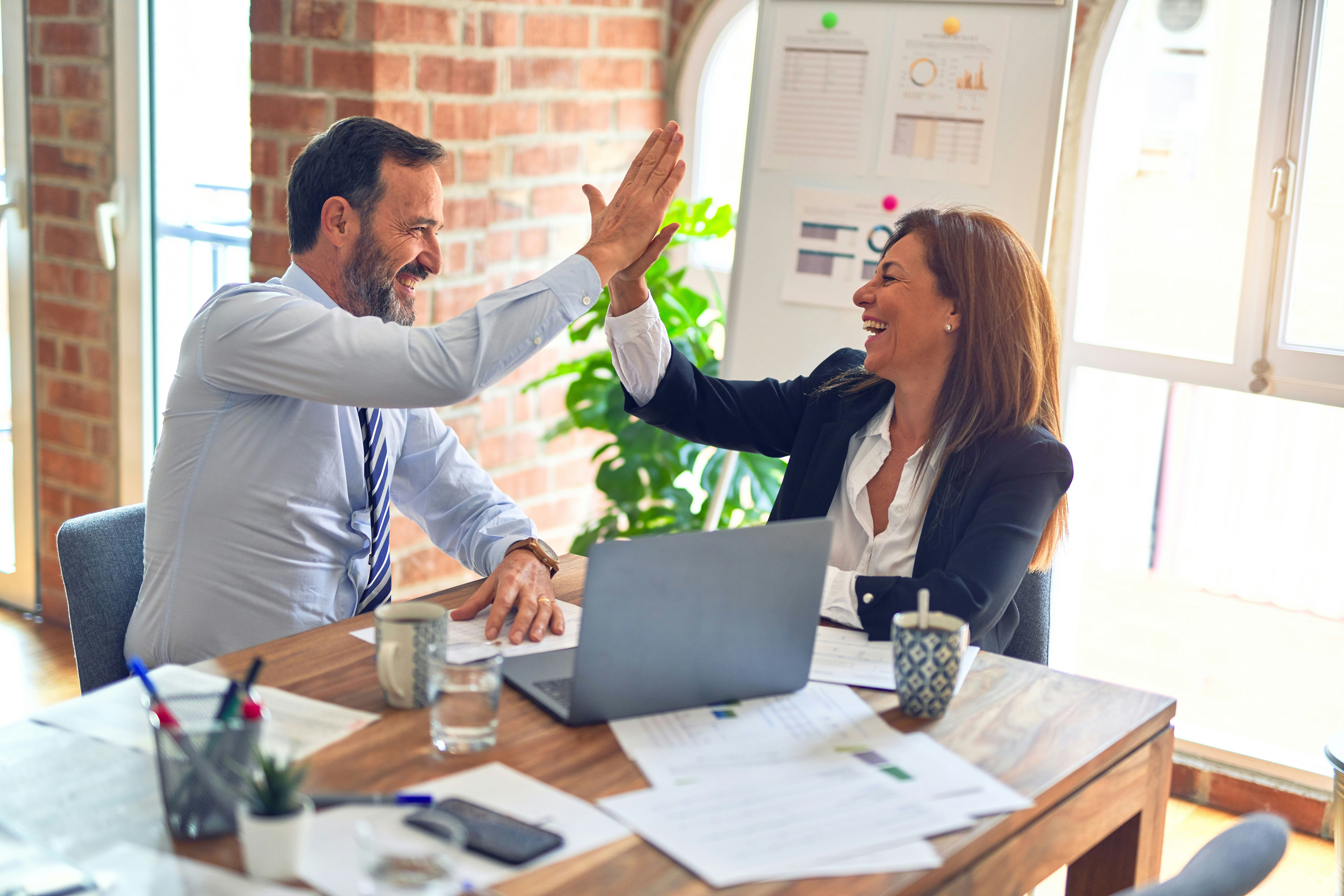 Two business professionals high-fiving at a desk in an office.