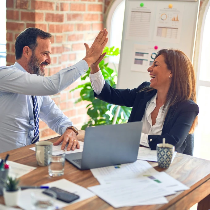 Two business professionals high-fiving at a desk in an office.