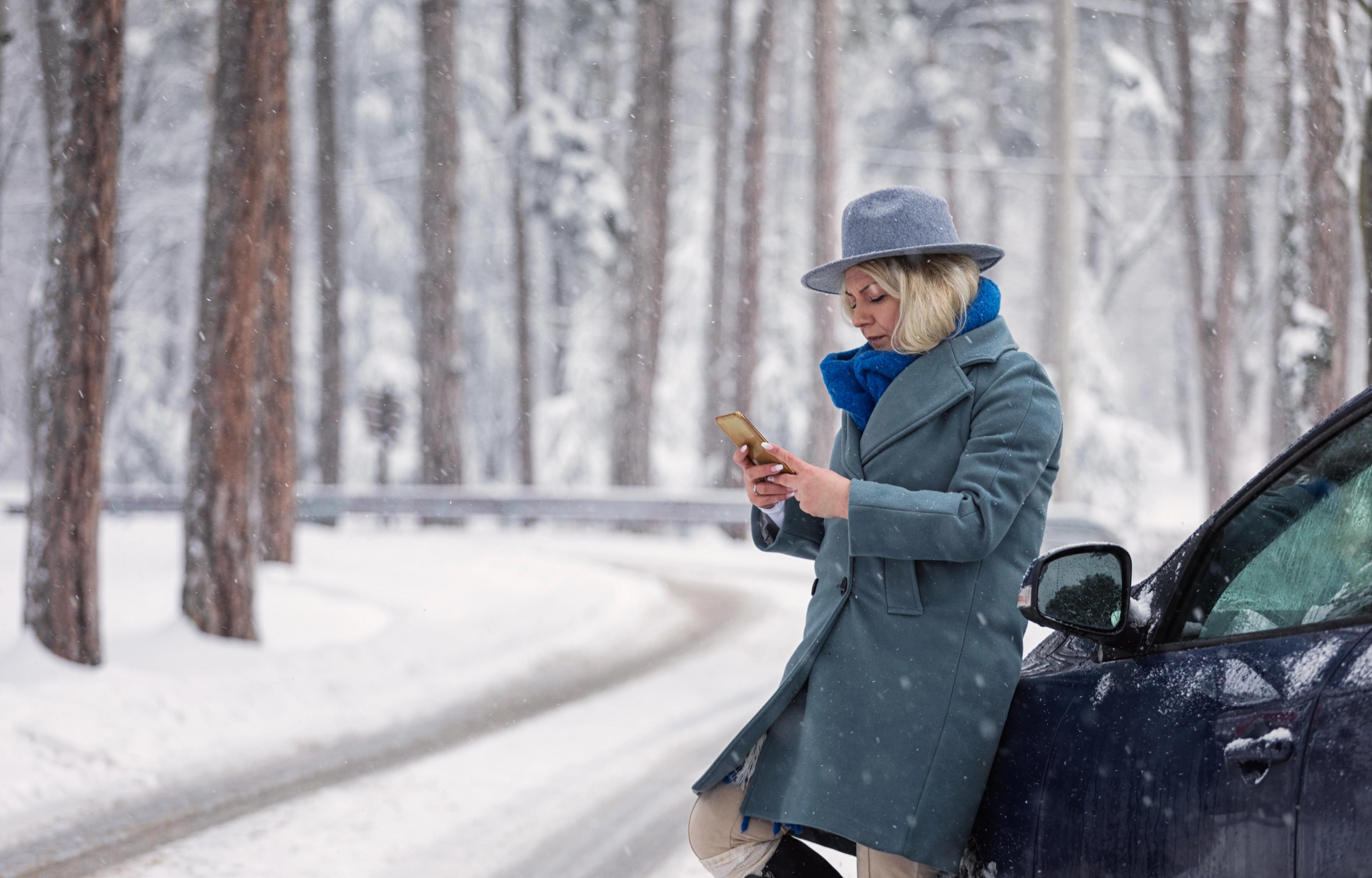 Woman sitting on car looking at phone