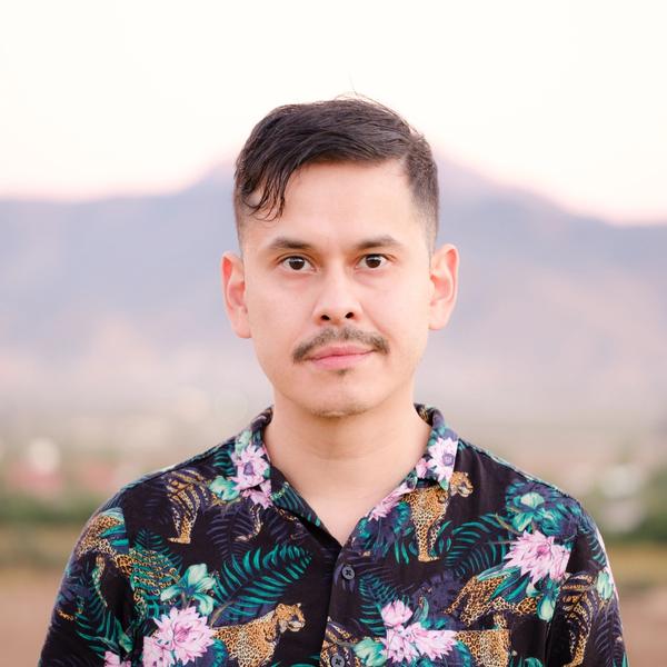 Headshot of Ray Luna standing in front of a mountain at dusk. He is wearing a tropical print shirt.
