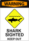 A sign with bold red text at the top that says "Warning", and iconography that indicates the presence of a shark. Text under the icon says: "Shark sighted. Keep out."