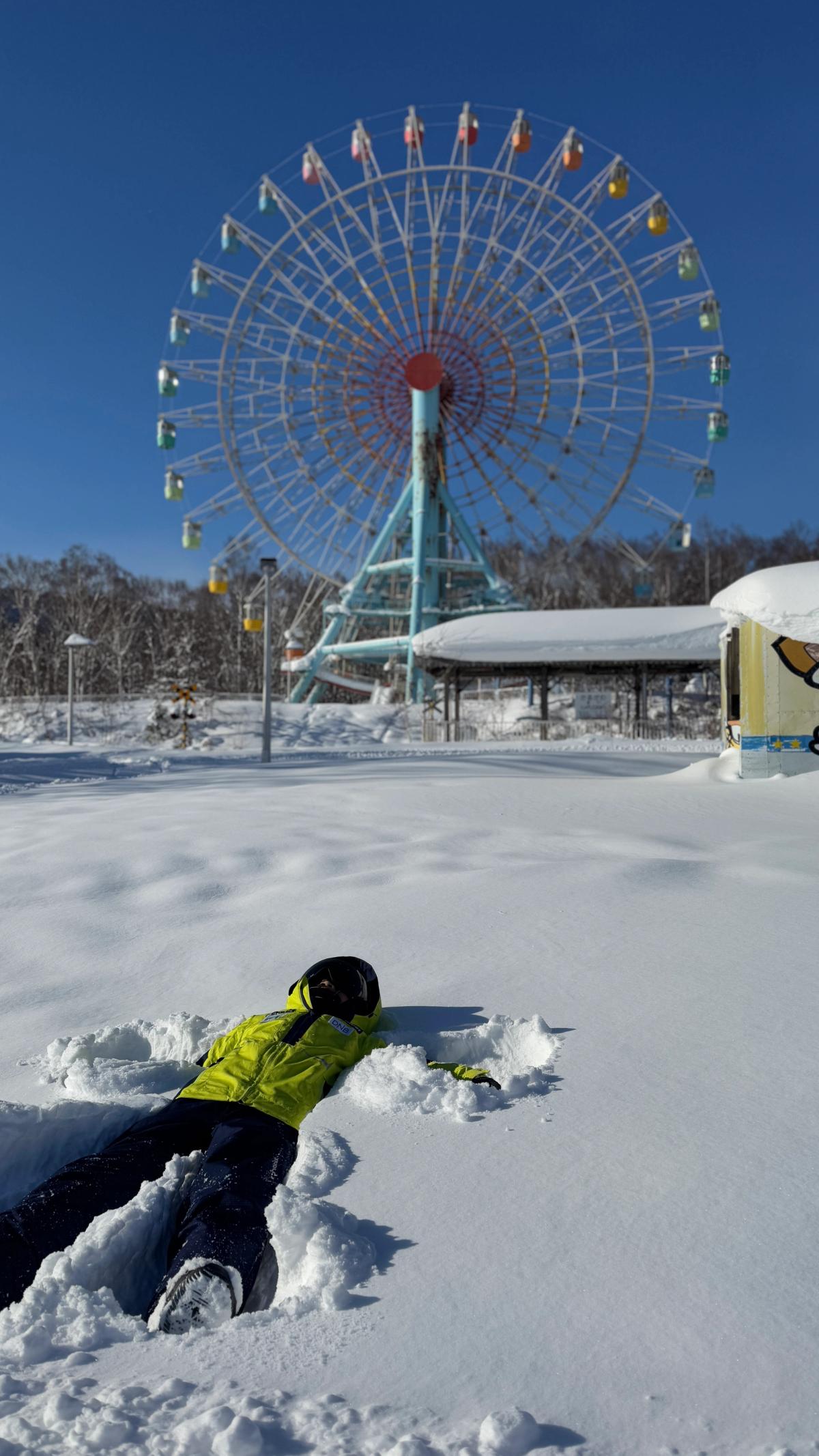 手稻奥林匹亚区的彩色摩天轮，前方雪地上有人躺着做雪天使