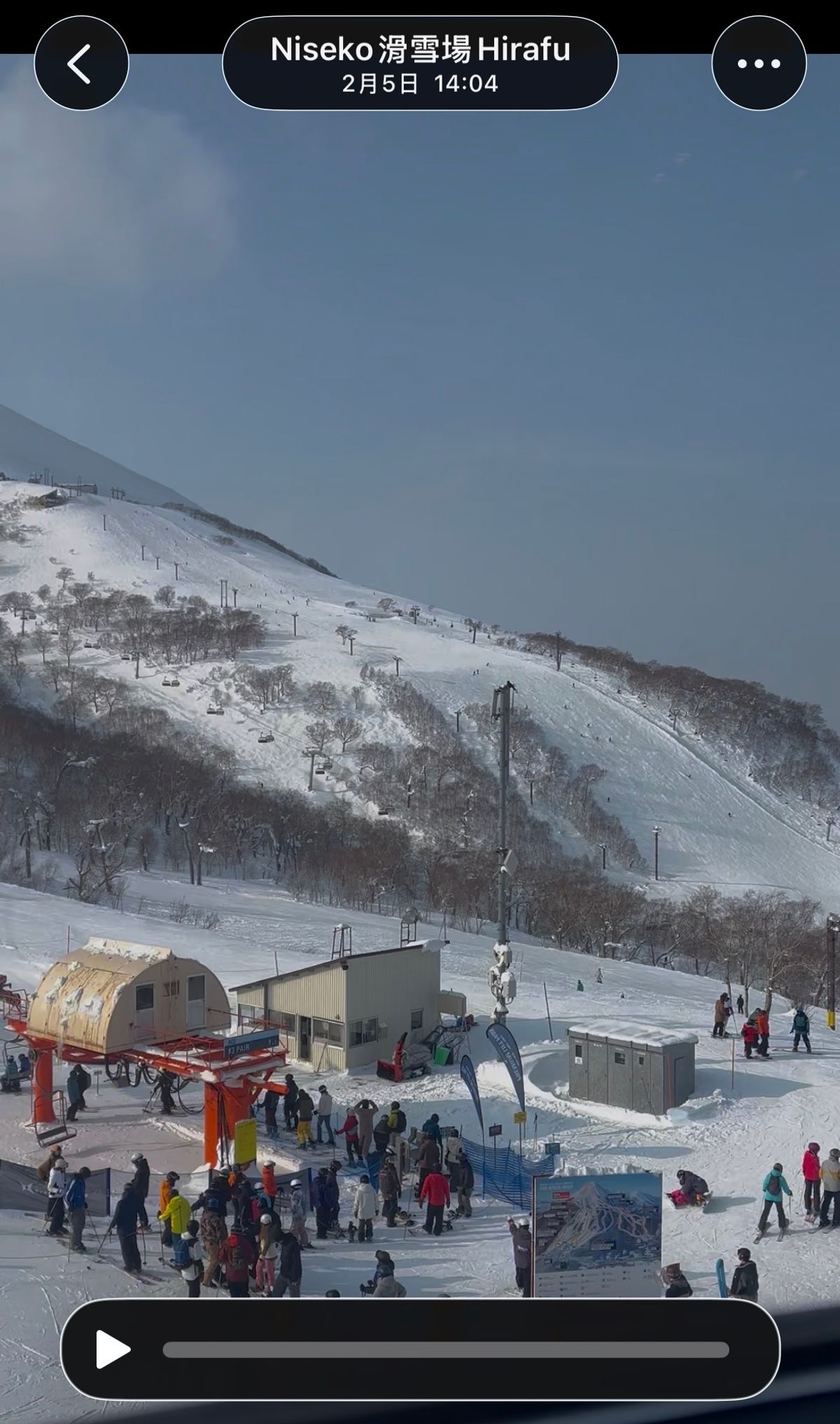 A crowded lift base at Niseko Hirafu with skiers queueing, tracked-out slopes behind. The capture stamp on the image reads 5 February, 14:04