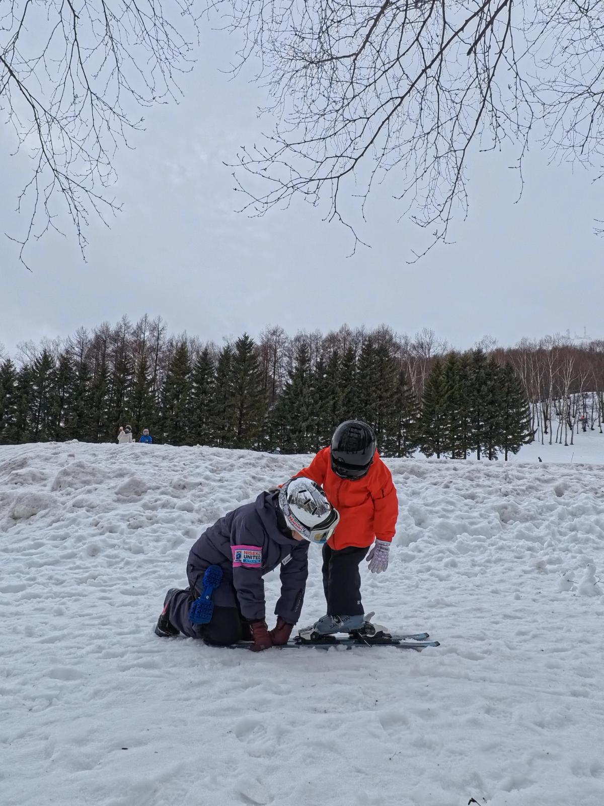 教練蹲在雪地上協助小朋友把雙板穿好