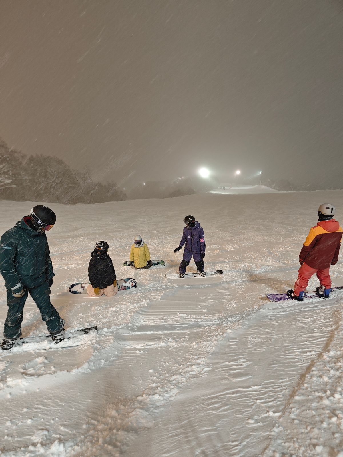 夜滑時段飄雪中，一組單板學員在雪道上跟著教練練習