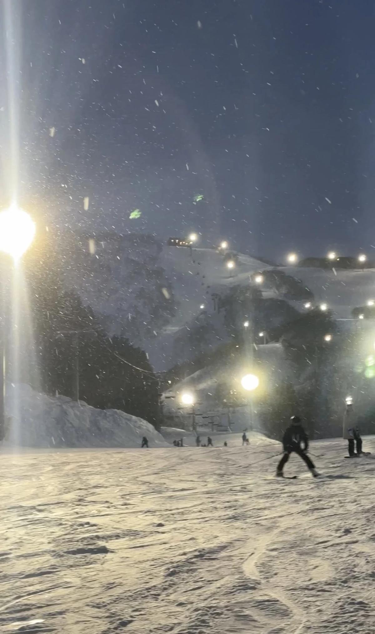 夜晚的初級雪道,幾位單板滑雪者坐在坡上看山下燈火,雪道空曠