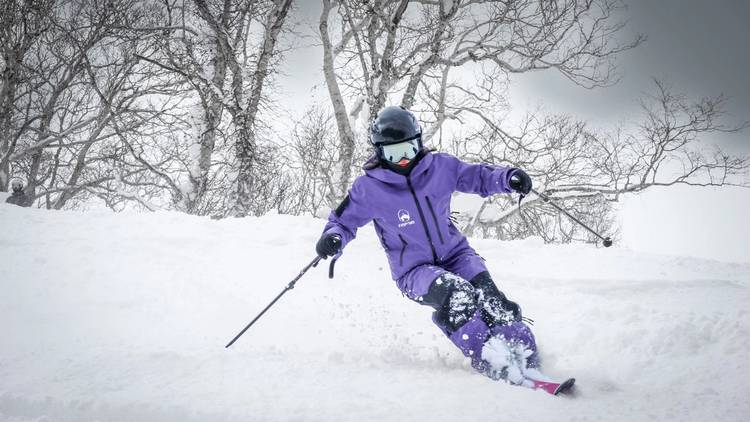 穿 FUYU 紫色制服的教練在樹林旁的粉雪裡轉彎
