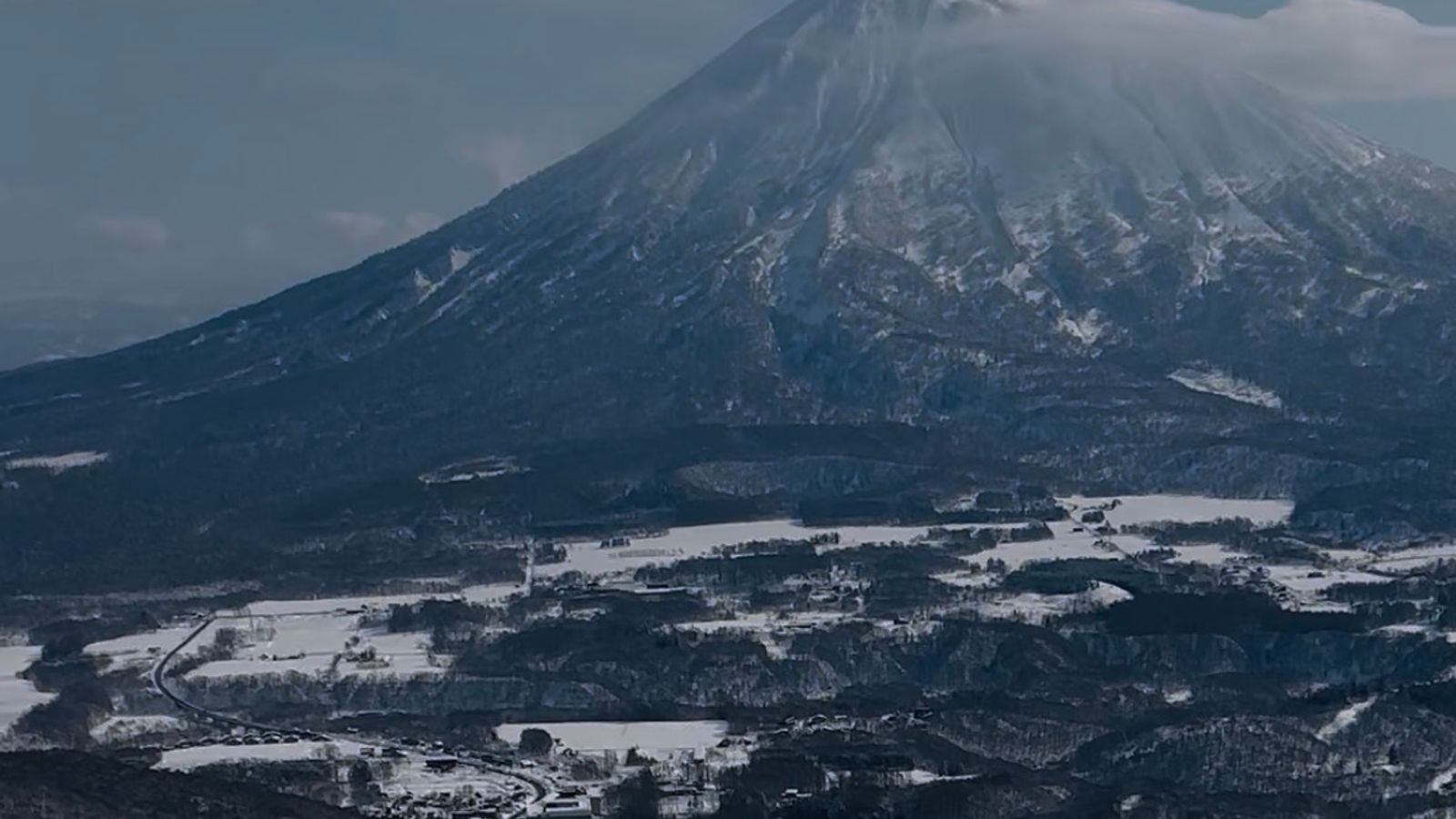 A skier dropping into a wide groomed slope with Mount Yotei filling the horizon behind the valley