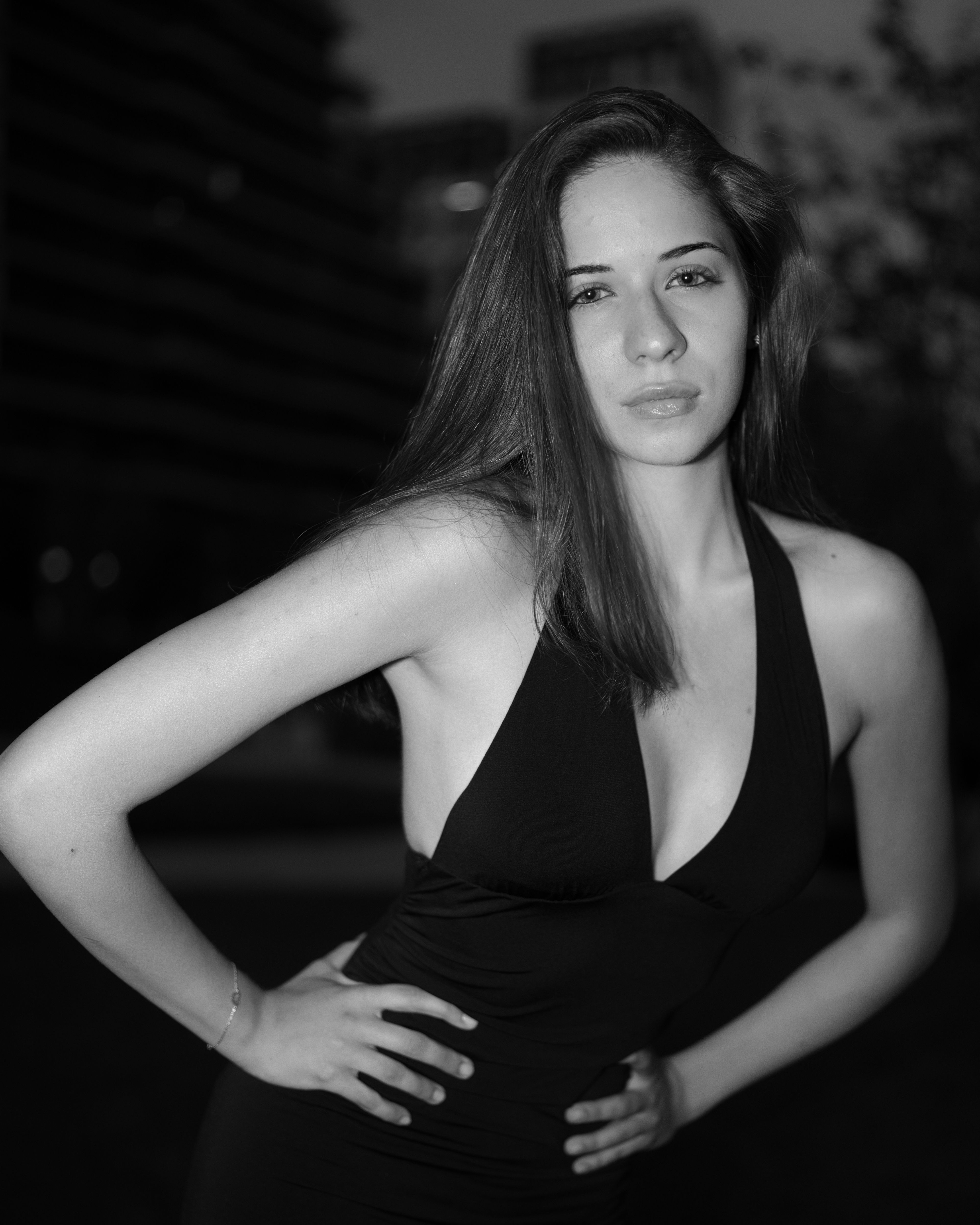 Monochrome portrait of a woman in a black dress posing dynamically against a dark urban backdrop.