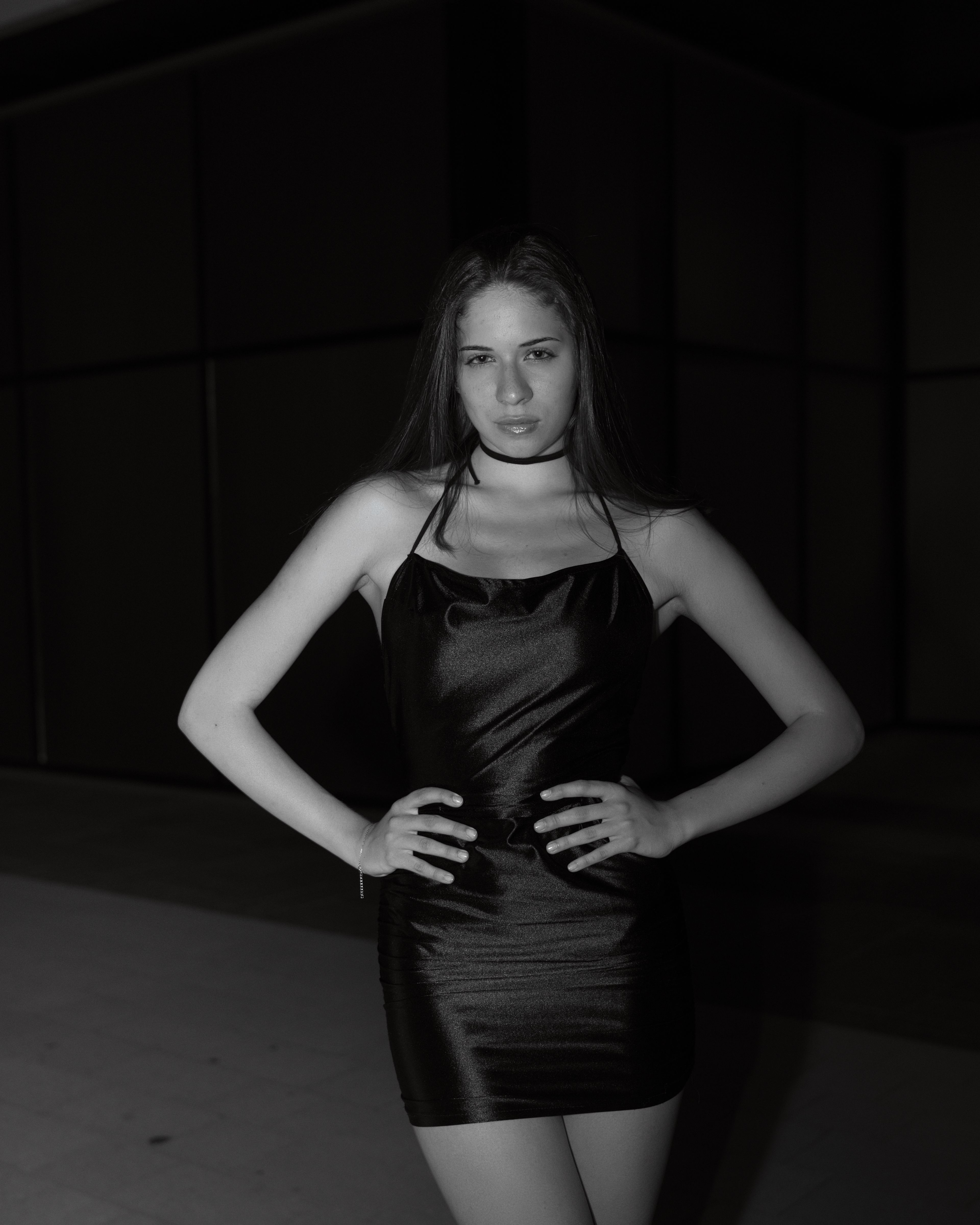 Black-and-white close-up portrait of a woman standing outdoors at night, gently resting her hand over her face with dramatic lighting.