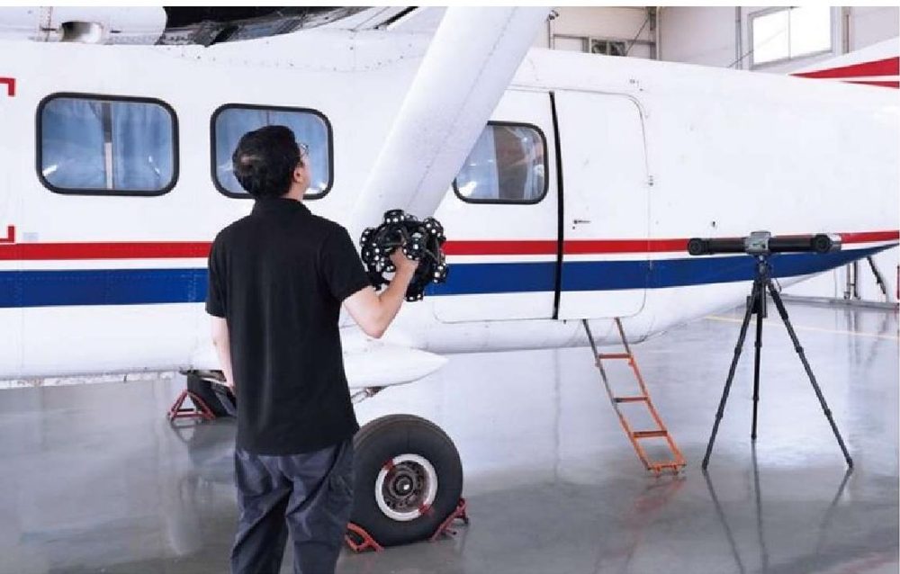 Technician using a handheld 3D scanner on a small aircraft in a hangar