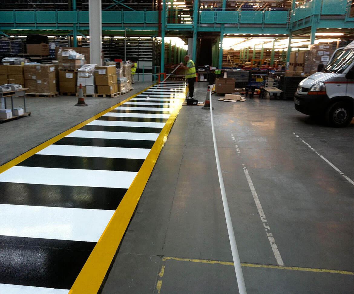 Warehouse floor with a painted yellow and white crosswalk and aisle lines