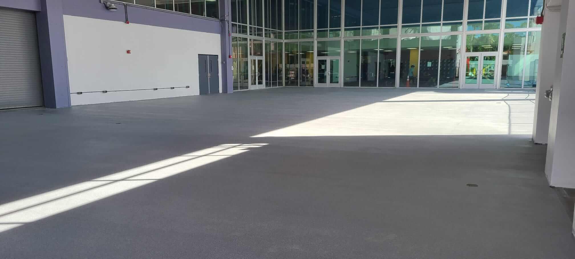 Gray coated concrete floor in a large empty building with a glass curtain wall