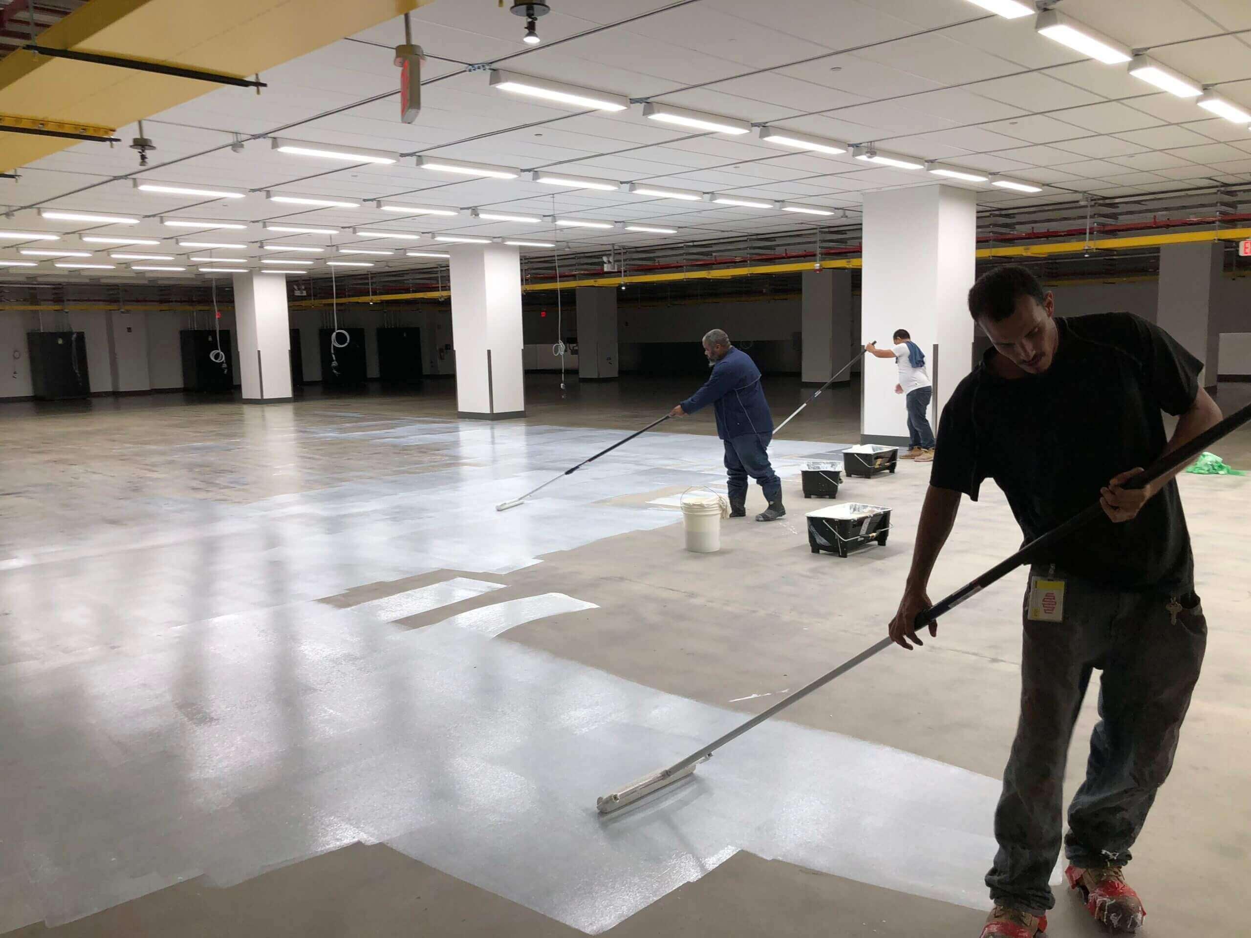Crew applying a floor sealer with squeegees in a large commercial space
