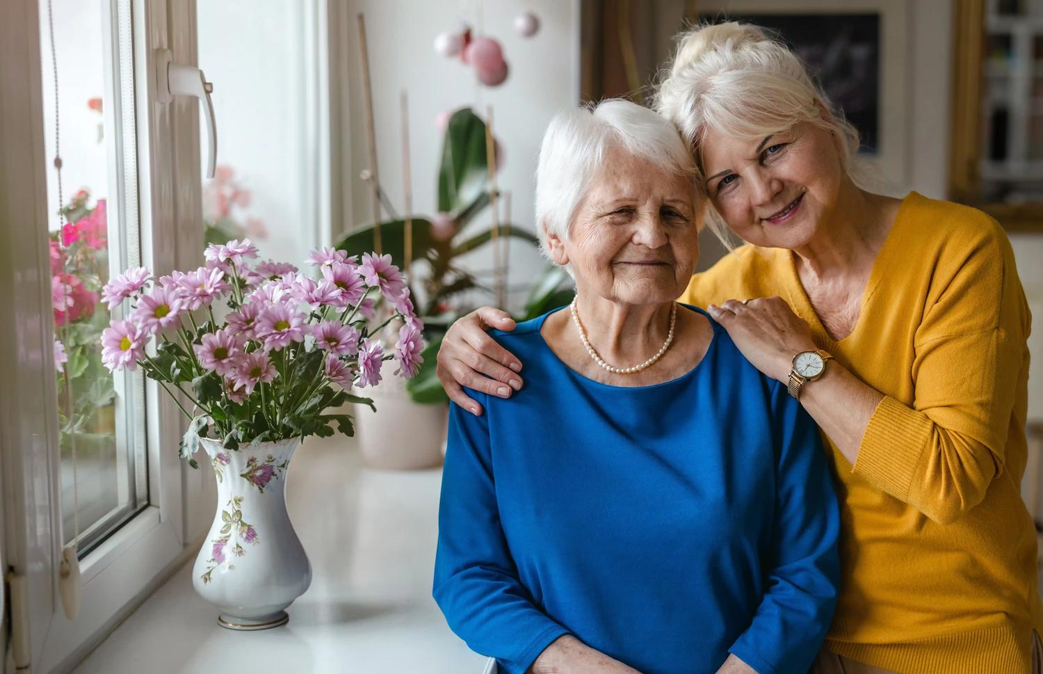 older woman hugged by daughter near window