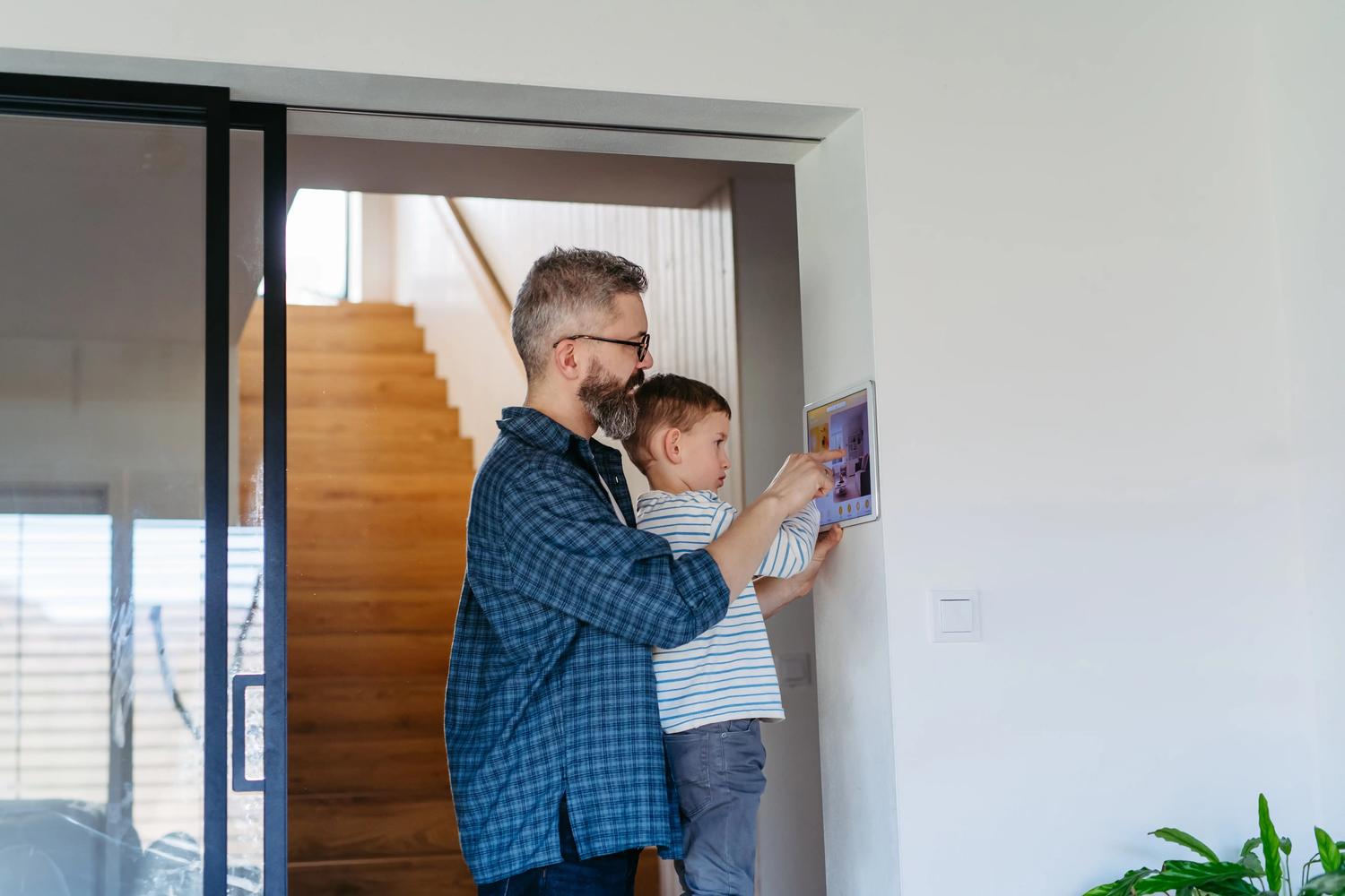 Father and son operating wall mounted home security system.