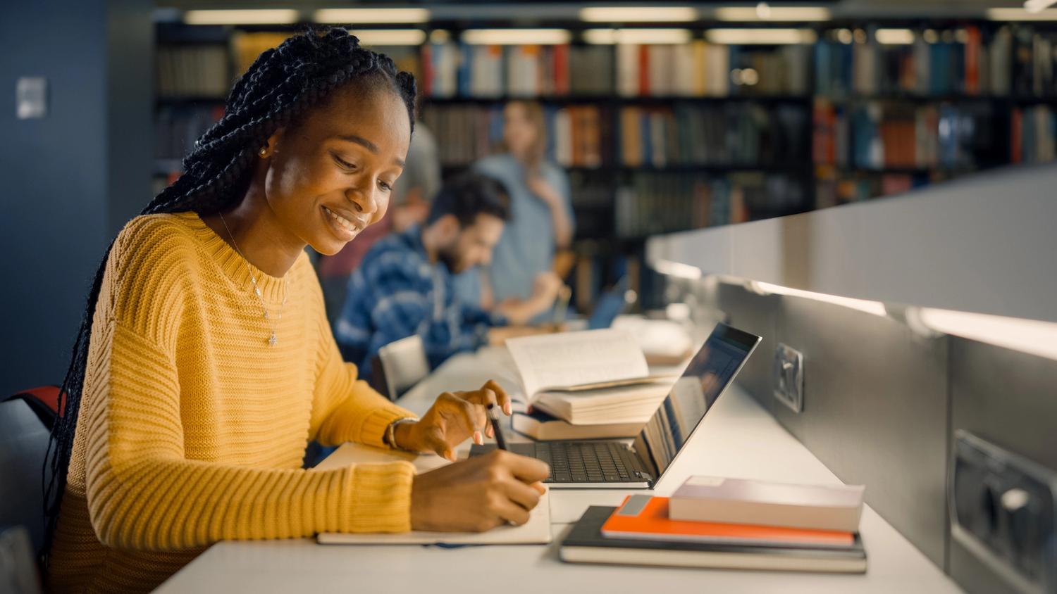 University Library: Gifted Black Girl uses Laptop, Writes Notes for the Paper, Essay, Study for Class Assignment.