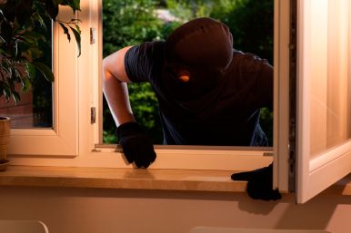 Burglar with his face hidden and sneaking through a window