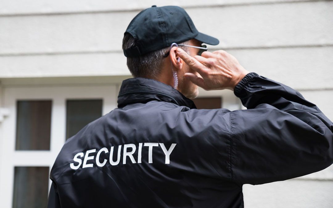A man in a security jacket and hat talking with an earwig.