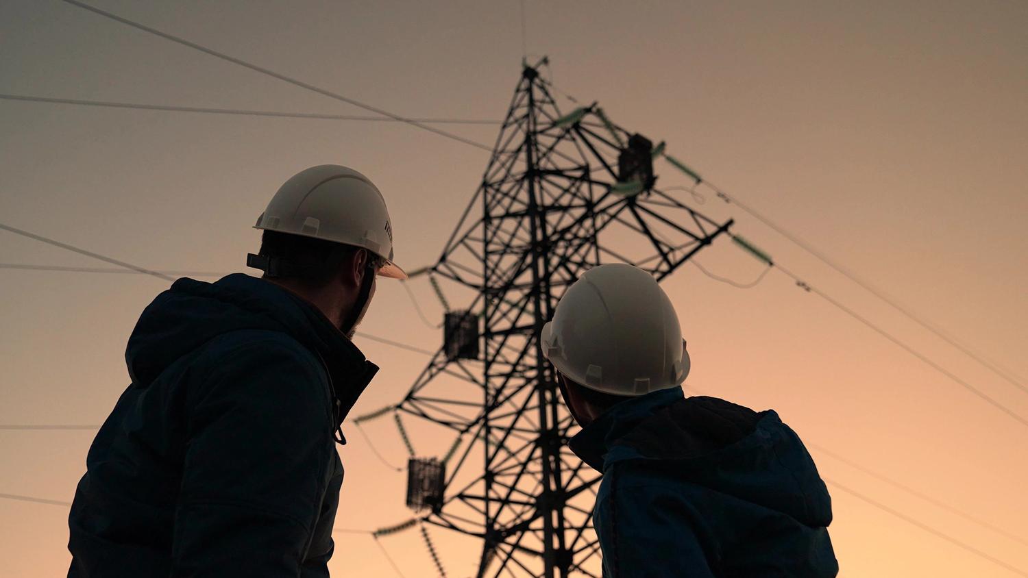 Two workers monitoring powerlines at sunset.