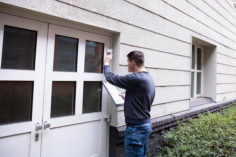 A man holding a checklist and checking the exterior doors of a building