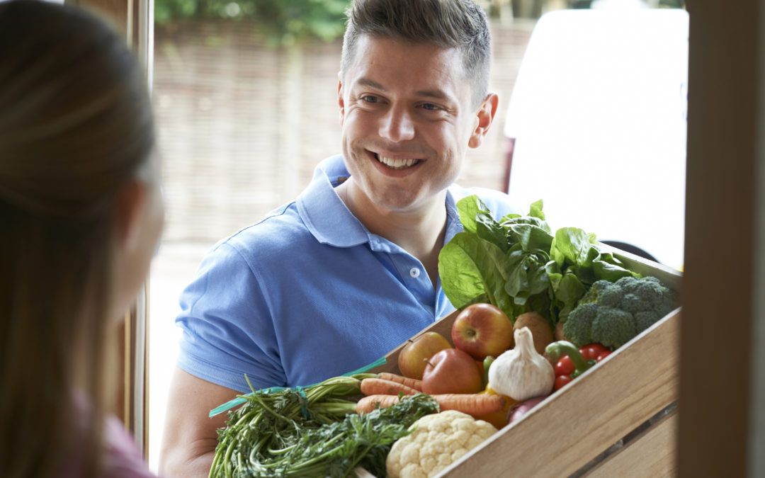 Blue shirt man talking to a lady while carrying a box of fruits and vegetables