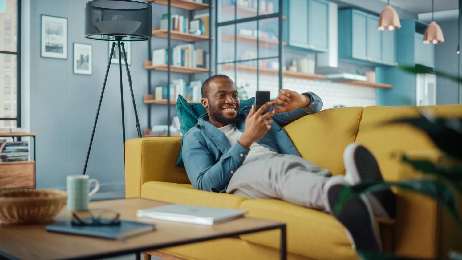 man laying on couch smiling at phone