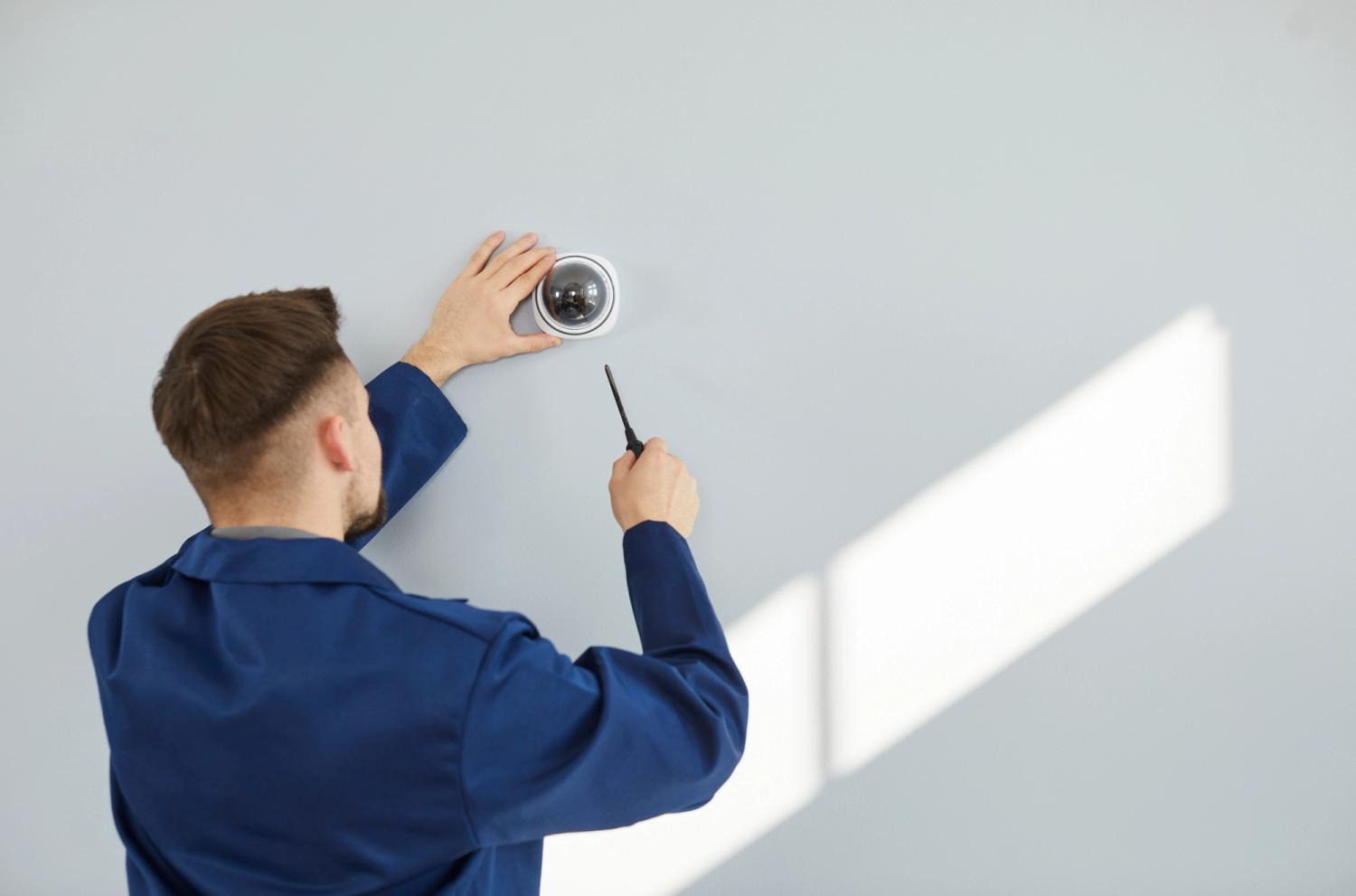 Electrician in blue jumpsuit installing CCTV 
