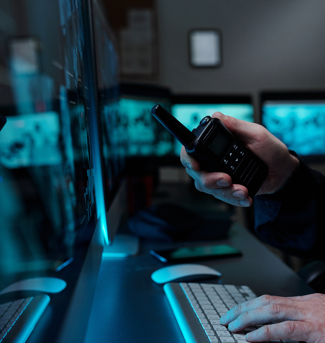 Close up of a hand holding a walkie talkie while monitoring security feeds