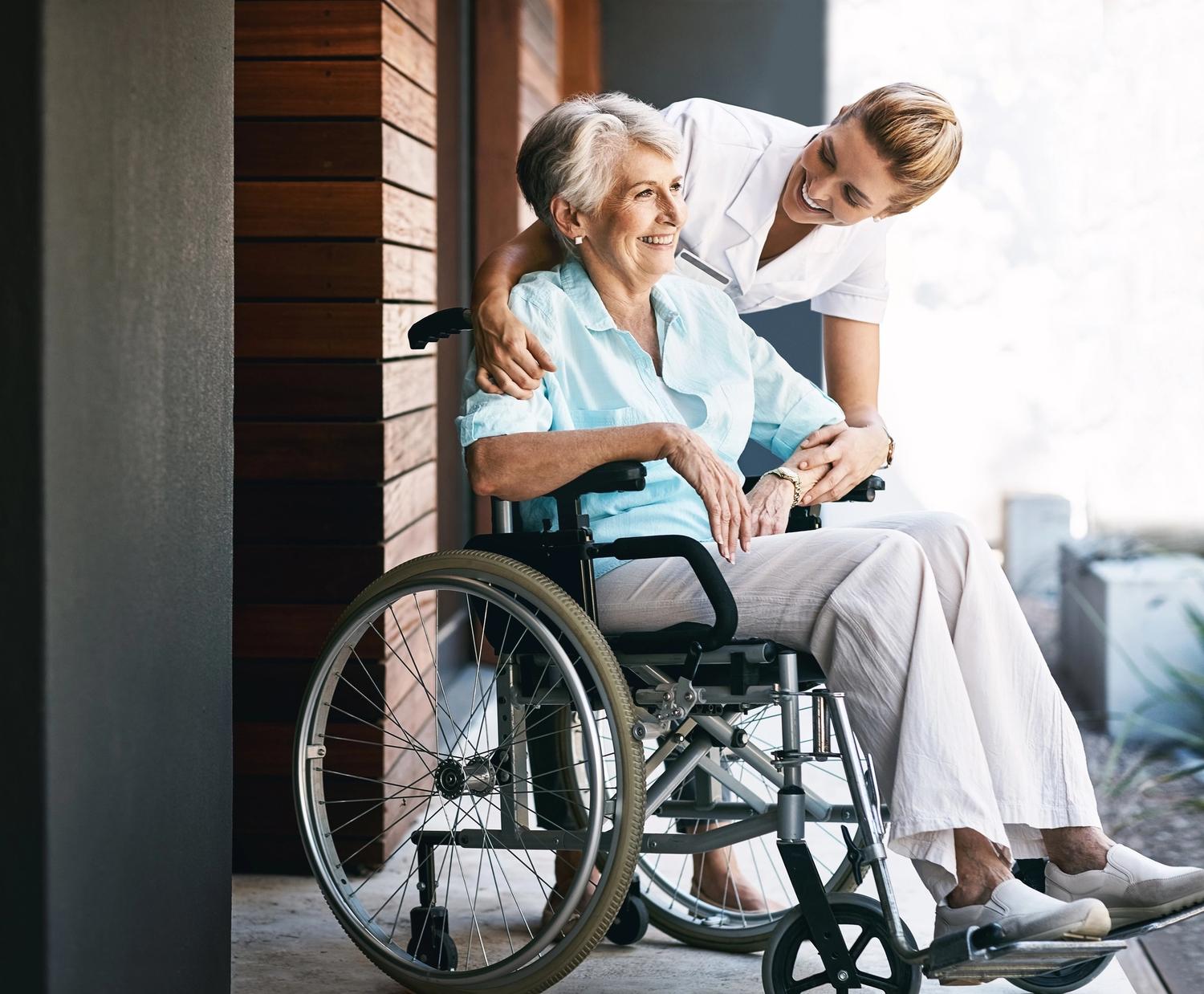 carer leaning over woman in wheelchair smiling