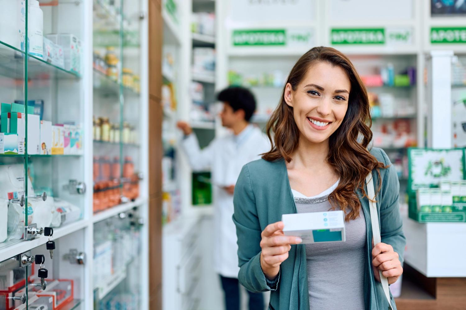 Customer at a pharmacy smiling and holding a box of medicine