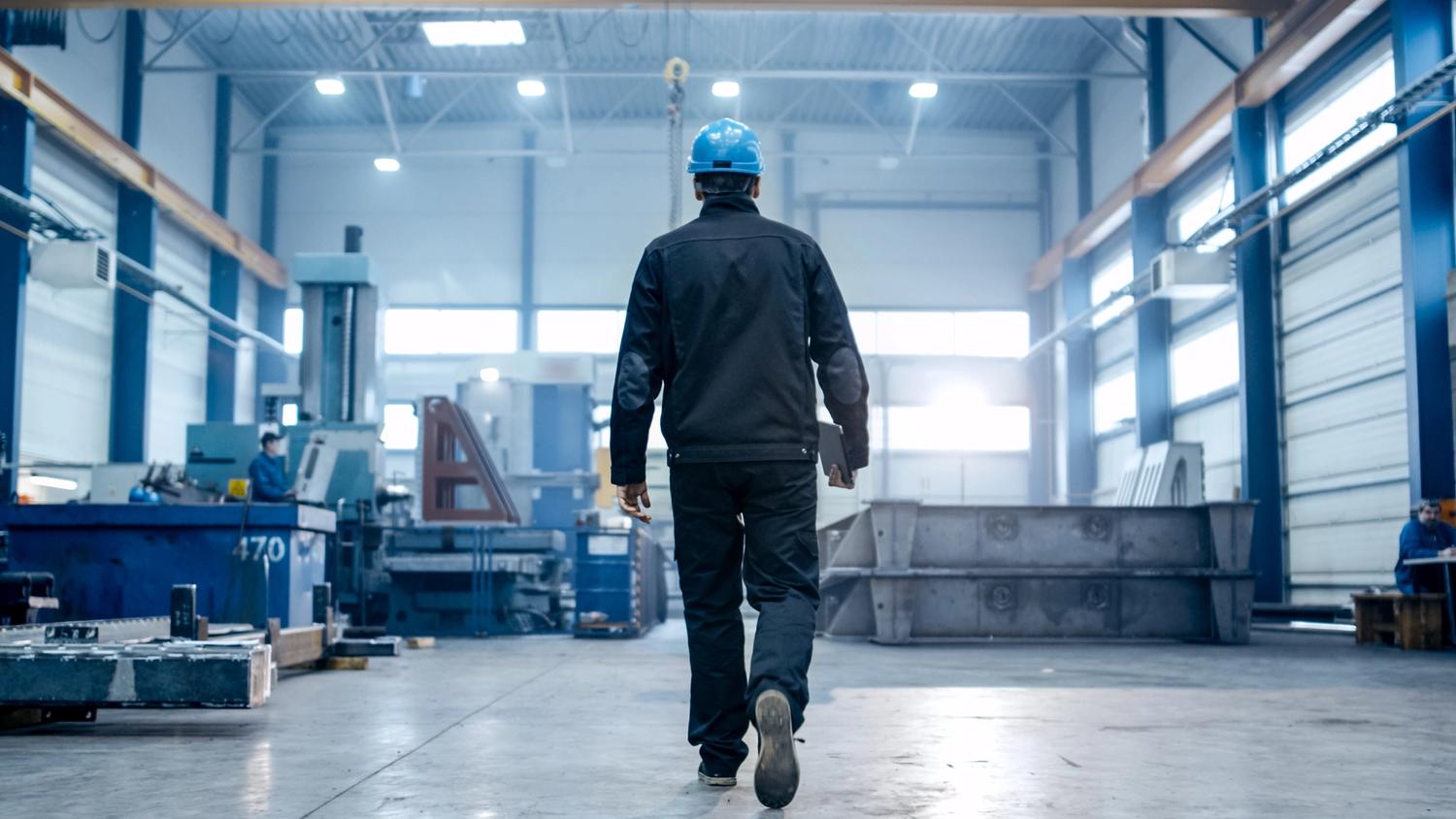 Factory worker in a hard hat is walking through warehouse