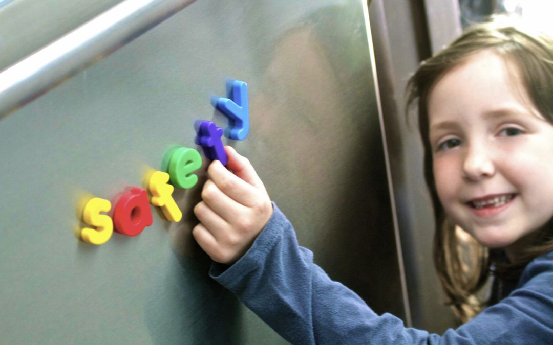 Little girl using alphabet magnets on a board to spell out safety