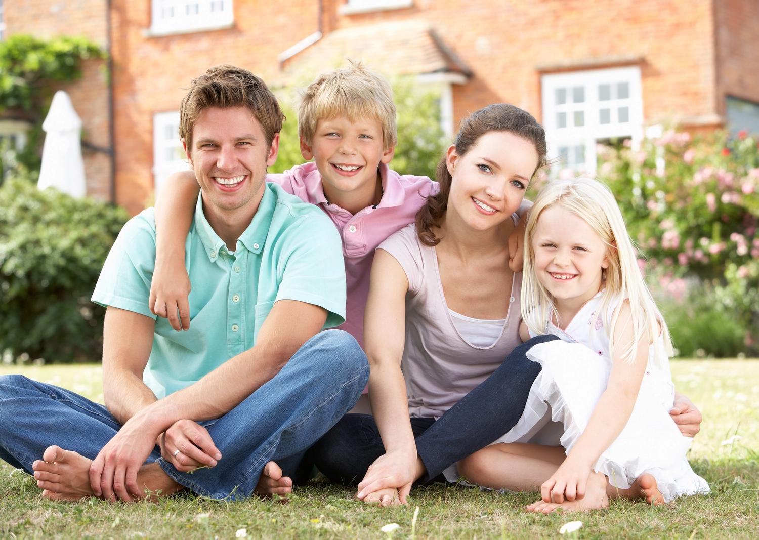 family of four sitting on the front lawn smiling