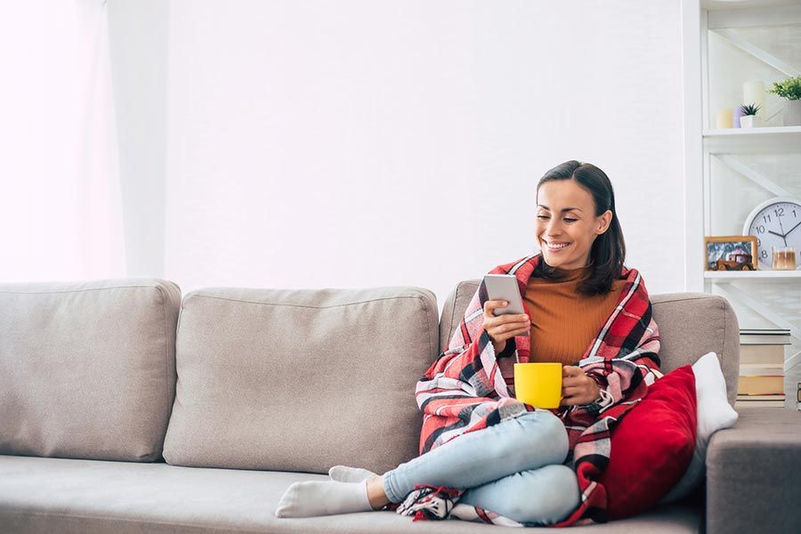 Smiling lady sitting on a couch holding a mug and phone