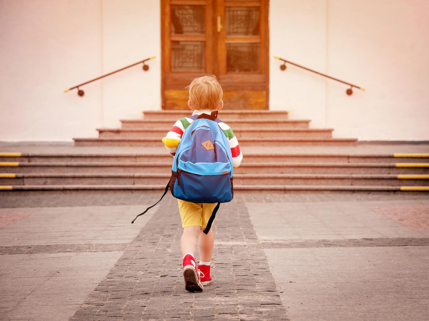back view of a child in a backpack walking to a building