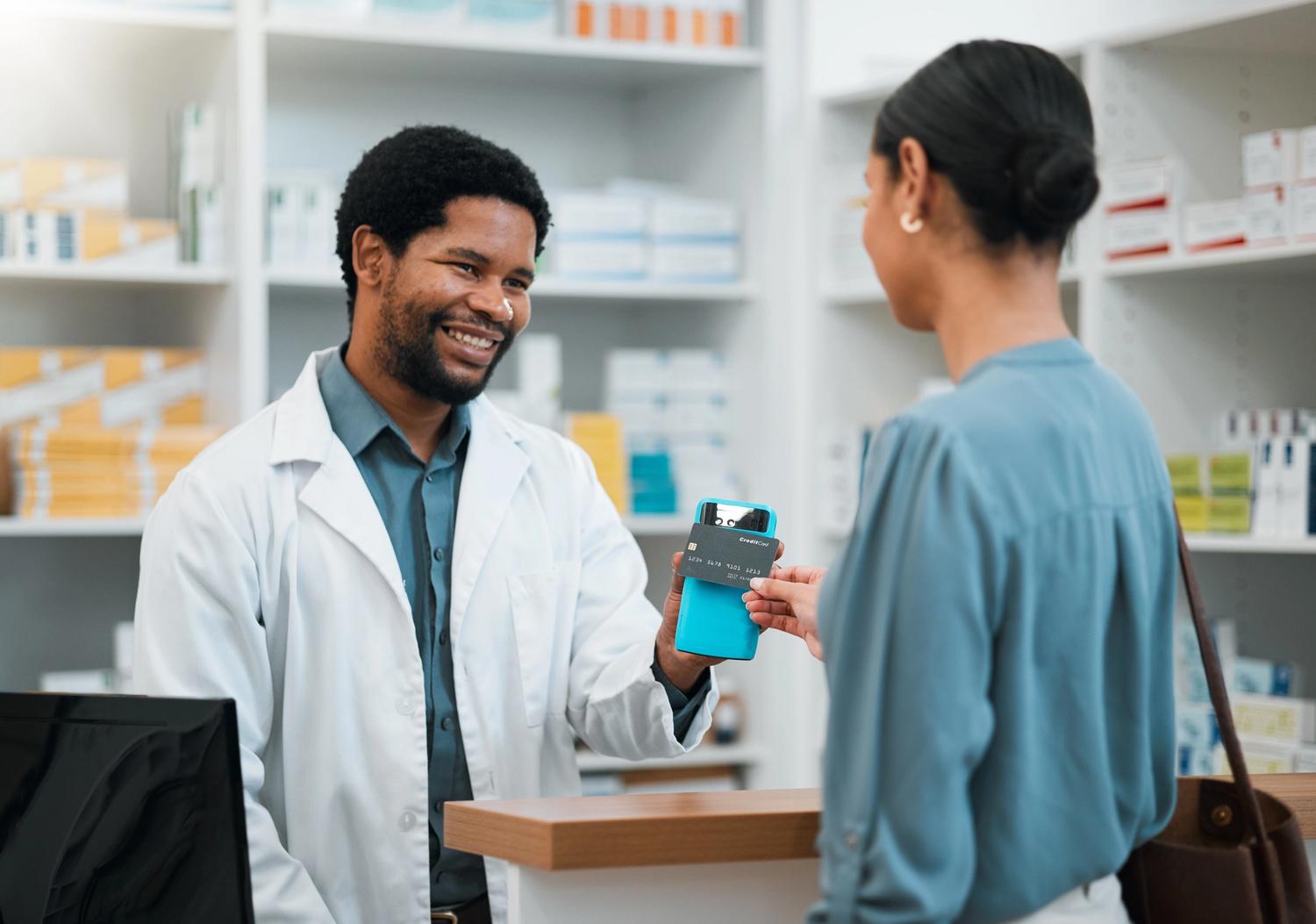 Male pharmacist holding a carder reader for a female customer to scan her card.