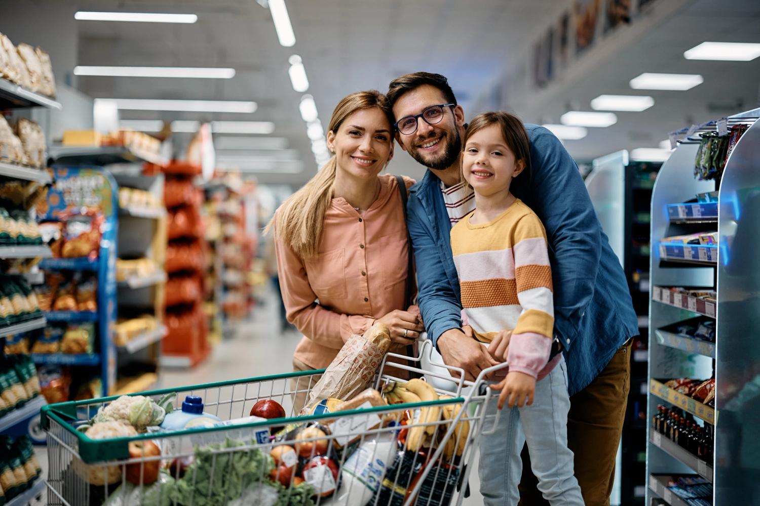 a smiling family in a supermarket with a trolley full of groceries