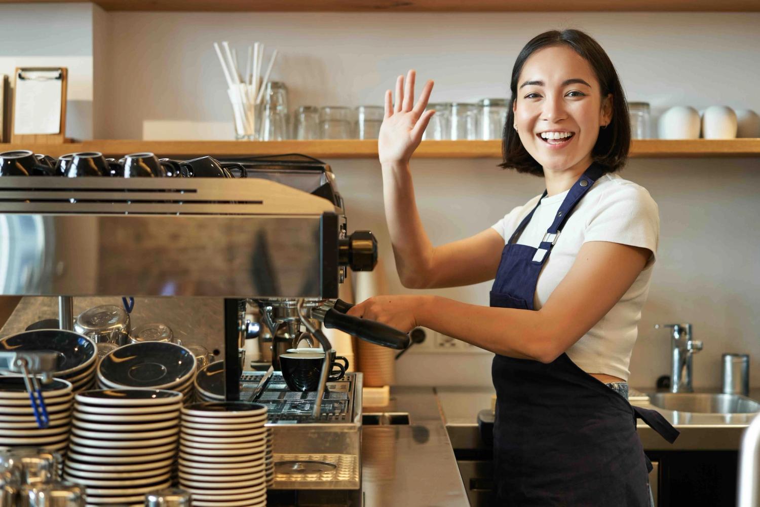 Woman waving at camera while making a coffee