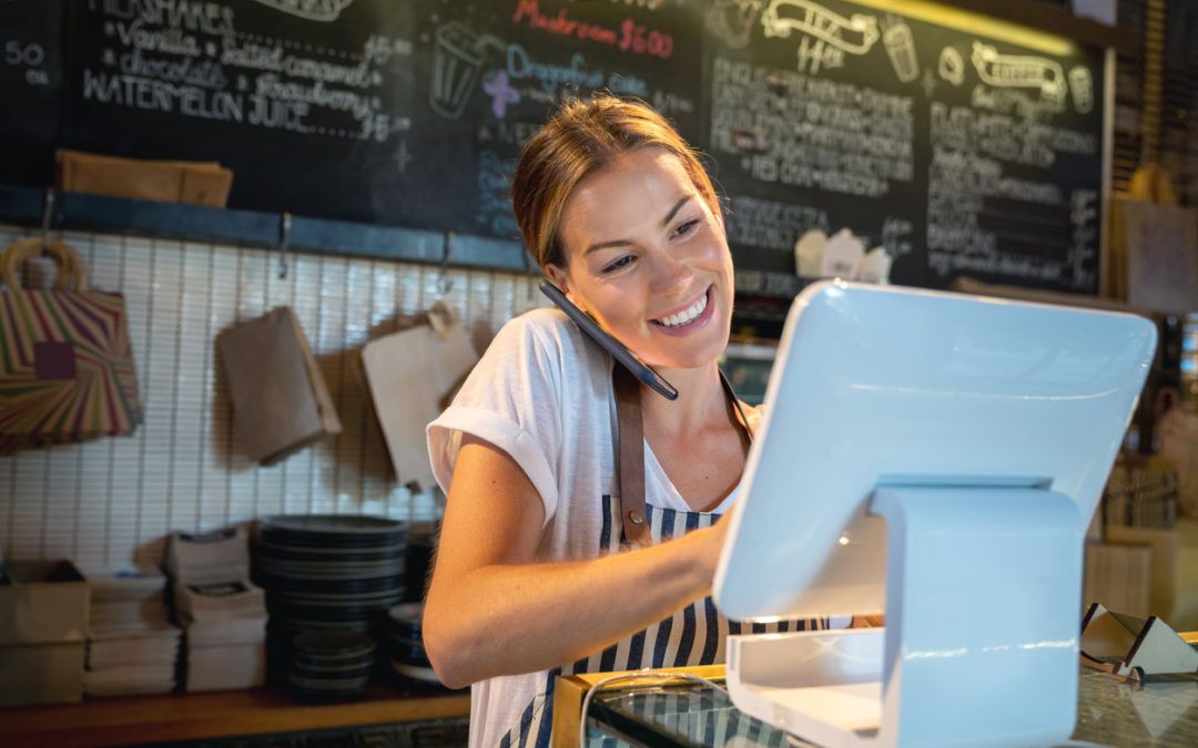 Female cafe worker behind a ordering computer and talking on phone