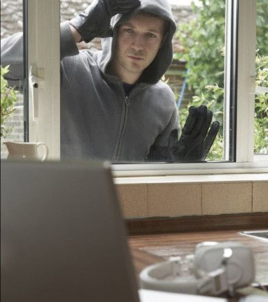 Grey hooded man looking through a house window, planning to break in